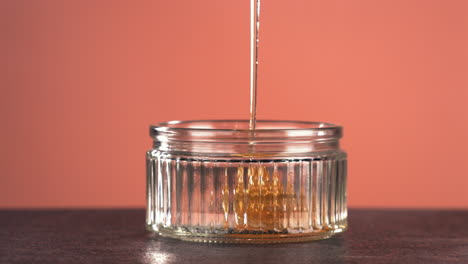 SUPER-SLOW-MOTION-CU-Honey-is-being-poured-into-glass-jar-against-bright-background